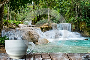 A white cup of coffee on the wooden table by the warterfall