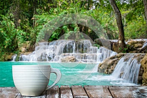 A white cup of coffee on the wooden table by the warterfall