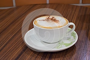 White cup containing hot cappuccino coffee on table