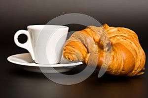 White cup and croissant on black background