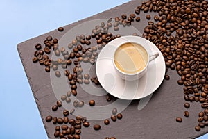 white cup with espresso coffee on a saucer with coffee beans on a dark and blue background