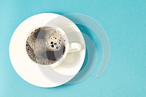white cup of espresso with a skin on a blue background/white cup with a saucer full of black coffee with a skin on a blue