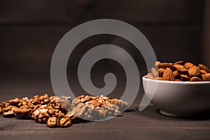 A white cup filled with almonds and scattered walnuts on a table