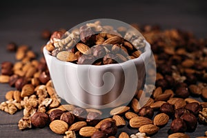 The white cup is filled with nuts. Hazelnuts, walnuts and almonds scattered around. Horizontal frame