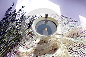 White Cup of fragrant tea with dried lavender flowers on a white openwork napkin, top view, on a pastel background in the sun rays