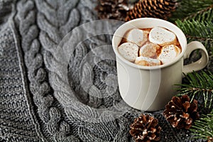 White cup of fresh hot cocoa or hot chocolate with marshmallows on grey knitted background