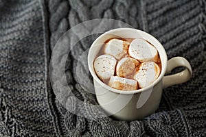 White cup of fresh hot cocoa or hot chocolate with marshmallows on grey knitted background