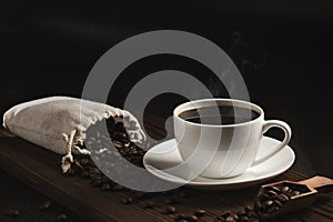 White cup of fresh hot coffee and coffee beans on wooden board on table