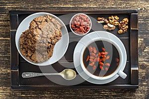 White cup of fresh morning goji coffee with cookies on wooden tray on the table, top view, close up