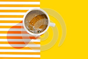 White cup of freshly brewed coffee with foamy crema on duotone yellow white striped background. Top view. Morning breakfast energy