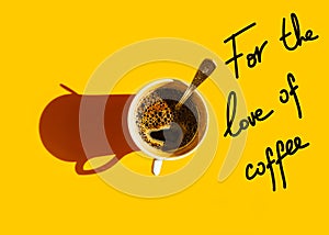 White cup of freshly brewed coffee with foamy crema tea spoon on solid yellow background top view. Hand lettering