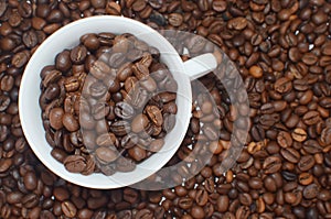 White Cup full of coffee beans on coffe beans background.