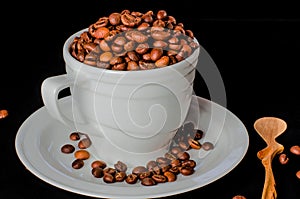 A white cup full of coffee beans stands on a white saucer, which stands on a black background