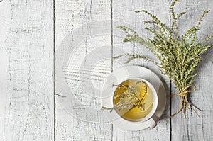 White cup of healthy herbal thyme tea with fresh thyme leaves bunch on white wooden rustic background