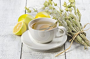 White cup of herbal sage tea with dried sage leaves and lemon on white wooden rustic background