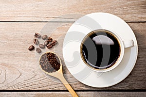 White cup of hot black coffee with coffee beans  on wood table background.