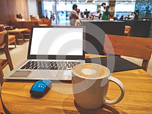 A white cup hot capuccino with white heart mug on top, a white screen computer labtop and blue mouse on brown wooden table