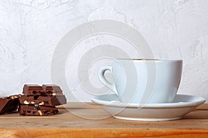 White cup of hot cocoa with marshmallows and some pieces of chocolate with nuts and raisin on wooden background.