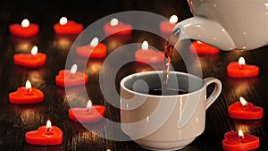 White cup with hot coffee on background of burning candles