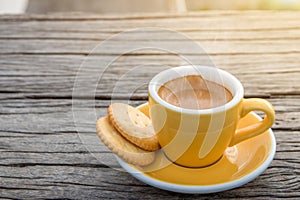 A white cup of hot espresso coffee mugs placed with cookies on a wooden floor with morning fog and moutains with sunlight