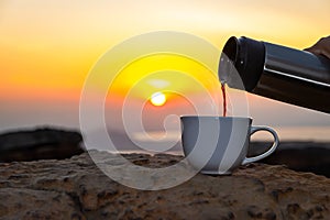 A white cup of hot espresso coffee mugs on the rocks and nature view of the sun background in the morning with sunlight