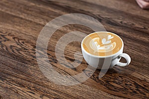 White cup of hot latte coffee with beautiful milk foam latte art texture isolated on wooden background. Overhead view