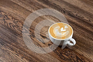 White cup of hot latte coffee with beautiful milk foam latte art texture isolated on wooden background. Overhead view