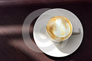 White cup of latte art coffee with shaped rosetta art on brown wooden table with copy space