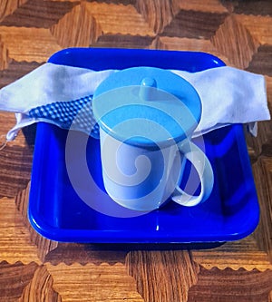 a white cup with a light blue lid on a dark blue tray with a white dishcloth on a brown checkered tablecloth