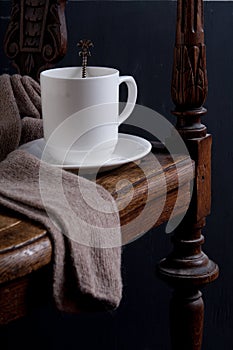 White cup on the old armchair with scarf  in dark key close up