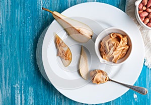 White cup with peanut butter. On a large white plate with a sliced â€‹â€‹pear..Flat lay composition. View from above. Blue wooden