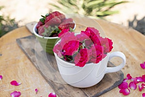 White cup with pink roses and green bowl with strawberries lying on stylish wooden board.