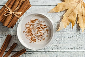 White cup of salep milky hot drink of Turkey with cinnamon powder and sticks healthy spice and autumn winter leaf on white rustic photo