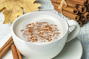 White cup of salep milky hot drink of Turkey with cinnamon powder and sticks healthy spice and autumn winter leaf on white rustic