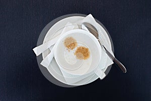 White cup with sapuchino coffee, on a saucer, with sugar and a spoon, is on the table. view from above