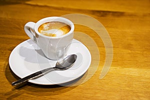 A white cup and saucer with coffee on a brown wooden table.