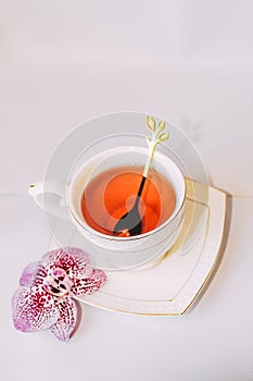 White cup with saucer and golden spoon and tea leaves.