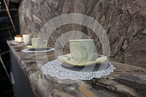 A white cup with a saucer and a lace napkin stands on a marble window sill