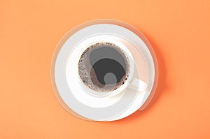 white cup with a saucer on a orange background/white cup of espresso with a foam on a orange background, top view