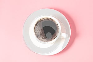 white cup with a saucer on a pink background/white cup of espresso with a foam on a pink background, top view