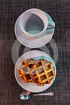 White cup on a saucer, spoon and round Viennese waffles on a white saucer