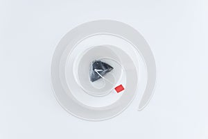 White cup and saucer with  tea bag inside. White background. View from above