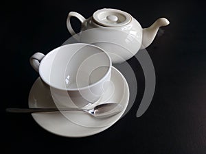 White cup and saucer and teapot isolated on black background