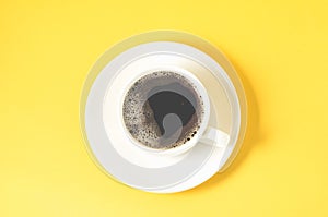 white cup with a saucer on a yellow background/white cup of espresso with a foam on a yellow background, top view