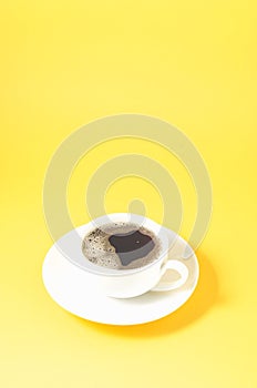 white cup with a saucer on a yellow background/white cup of espresso with a foam on a yellow background with copyspace