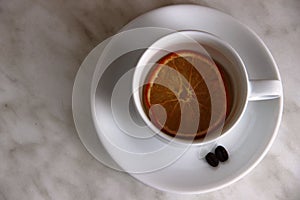 White Cup with slice of dried orange and a couple an coffee beans on a gray table