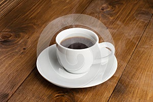 White cup of steamy coffee on wooden table