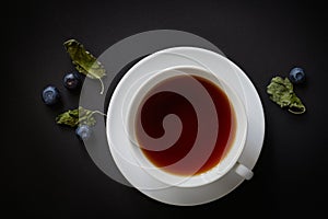 White cup with tea, blueberries and dried mint leaves