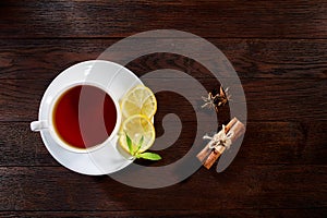 White cup of tea with cinnamon sticks, lemon, mint leaves and tea strainer on wooden rustic table.