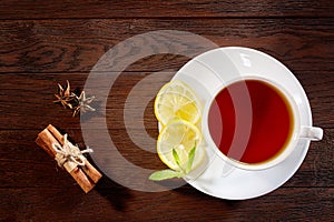 White cup of tea with cinnamon sticks, lemon, mint leaves and tea strainer on wooden rustic table.